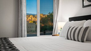 Habitación de hotel con una cama grande, vistas a las montañas y una ventana con cortinas.