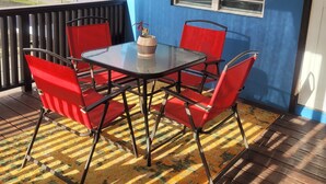 A covered outdoor seating area with a blue wall, a window with horizontal blinds, and a table with red chairs. - Silverbuttons  (St. John's)