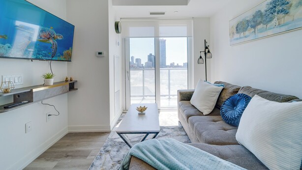 A modern living room with a large TV, a sofa, a coffee table, and a view of the city through large windows.