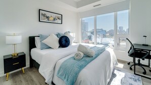 A modern hotel room with a large bed, a desk, and a view of the city.