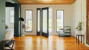 Une pièce spacieuse avec un plancher en bois, un banc noir et blanc, une petite table avec une plante, et une porte donnant sur un espace extérieur.
