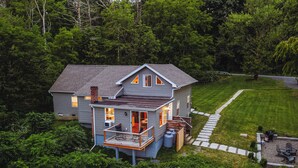 Une maison à deux étages dotée d’un balcon, entourée d’une végétation luxuriante.