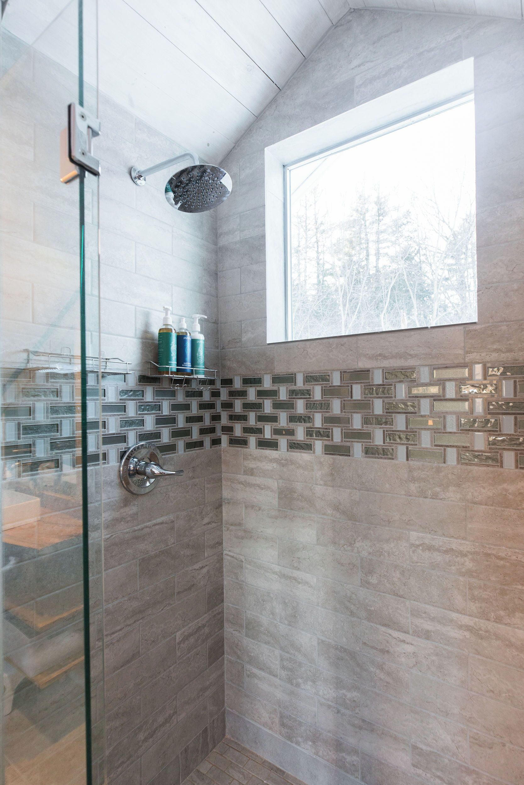 Eine Dusche mit Glastür, Fenster und einer Fliesenwand mit geometrischem Muster.