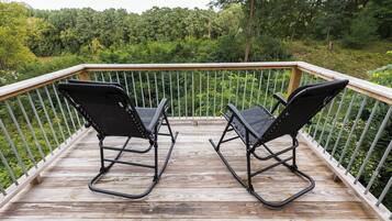 A wooden deck with two black rocking chairs facing a lush green forest.