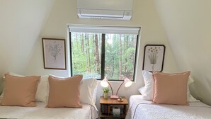 Una habitación acogedora con dos camas, una mesita con lámpara y ventana con vista al bosque.