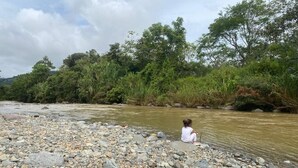A rocky riverbank with a person sitting by the water. - Magnolia Farm Suite
      Giffin House
       Pet friendly (San Isidro de El General)