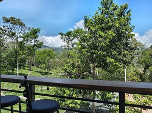 Une vue depuis un balcon doté d’une balustrade en bois, donnant sur un paysage verdoyant et luxuriant, avec des arbres et des collines.