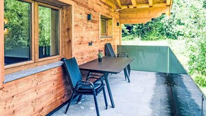 Una cabaña de madera con un porche cubierto, ventanas amplias y vistas al bosque circundante.