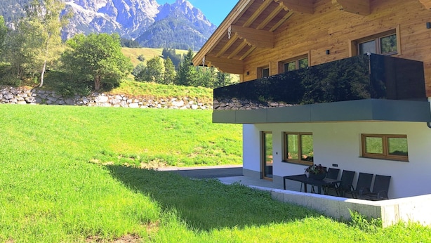 Una casa moderna de dos pisos con fachada de madera, un balcón y vistas a las montañas.