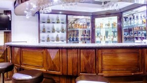 Un espace bar doté d’un comptoir en bois incurvé, de plusieurs tabourets et d’étagères remplies de bouteilles.