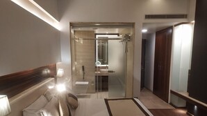 Une chambre d’hôtel moderne avec un grand lit, des lampes de chevet, une douche en verre et une armoire.