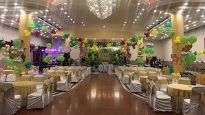 Une salle de banquet avec des tables rondes, des chaises blanches et des rubans dorés.