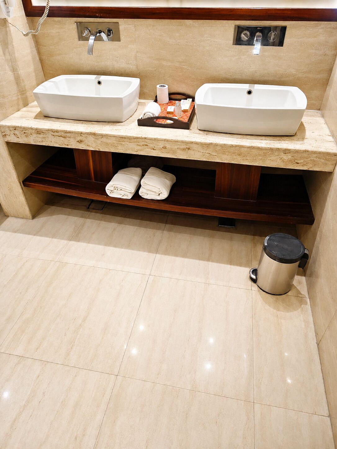 A bathroom with two sinks, a towel rack with towels, a toilet, and a trash can.