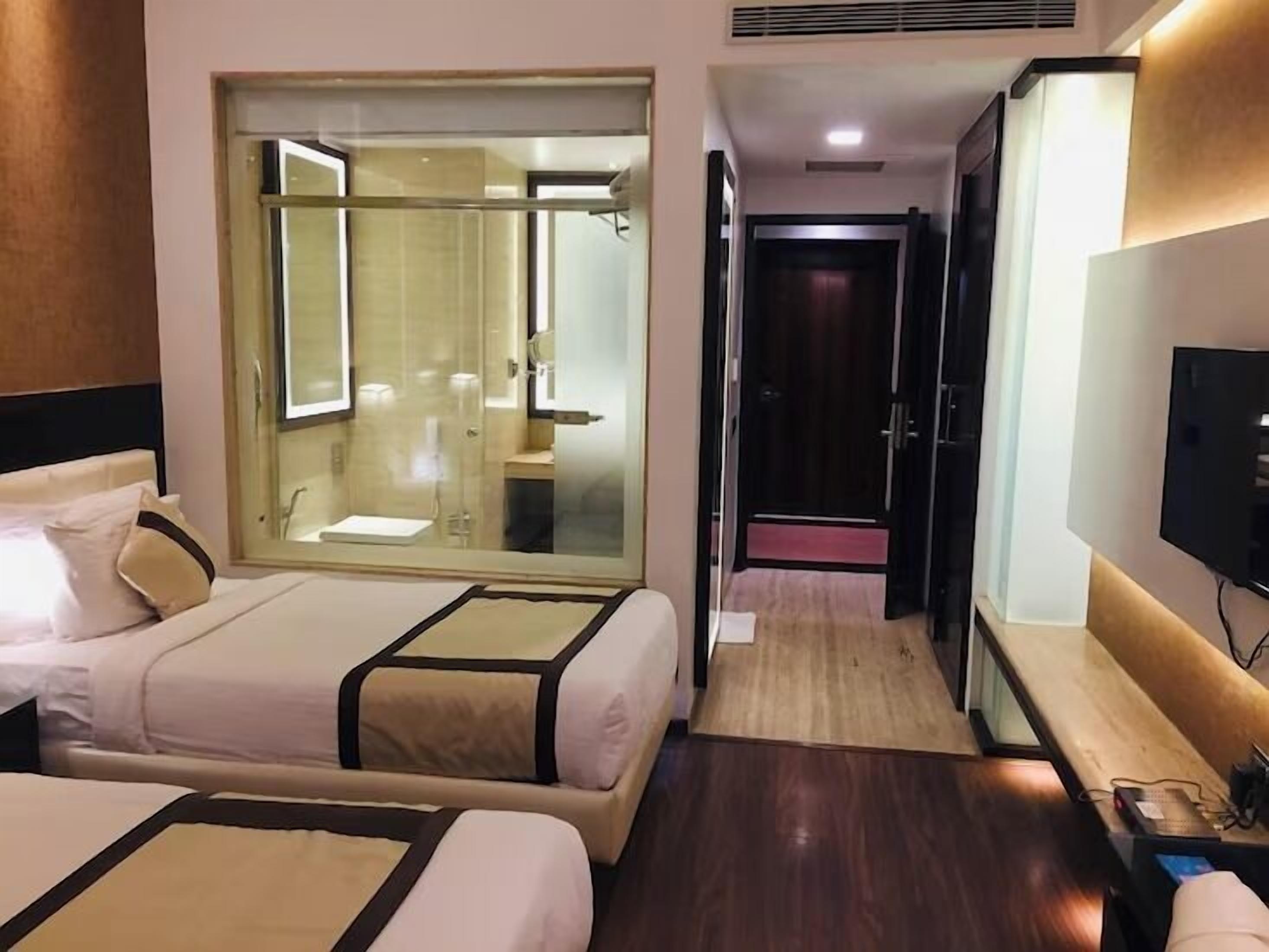 A hotel room with two beds, a glass-enclosed shower area, a television, and a wooden floor.