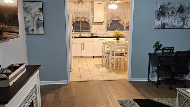 Une cuisine moderne avec des meubles blancs, un coin repas comprenant une table et des chaises, et un couloir menant au salon.
