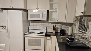 Une cuisine avec des meubles blancs, une cuisinière, un four à micro-ondes et un évier.