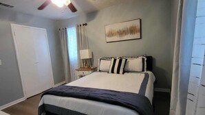 Une chambre à coucher avec un lit, un ventilateur de plafond, une table de chevet, une lampe et une porte.