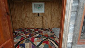 A small, cozy room with a wooden interior, a quilted bedspread, and a framed picture on the wall. - Charming Waterfront Tree House in Kaufman (Kaufman)