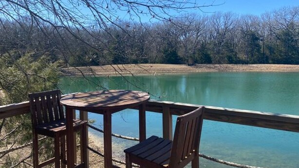 A wooden deck with a table and chairs overlooking a calm lake, surrounded by trees. - Charming Waterfront Tree House in Kaufman (Kaufman)