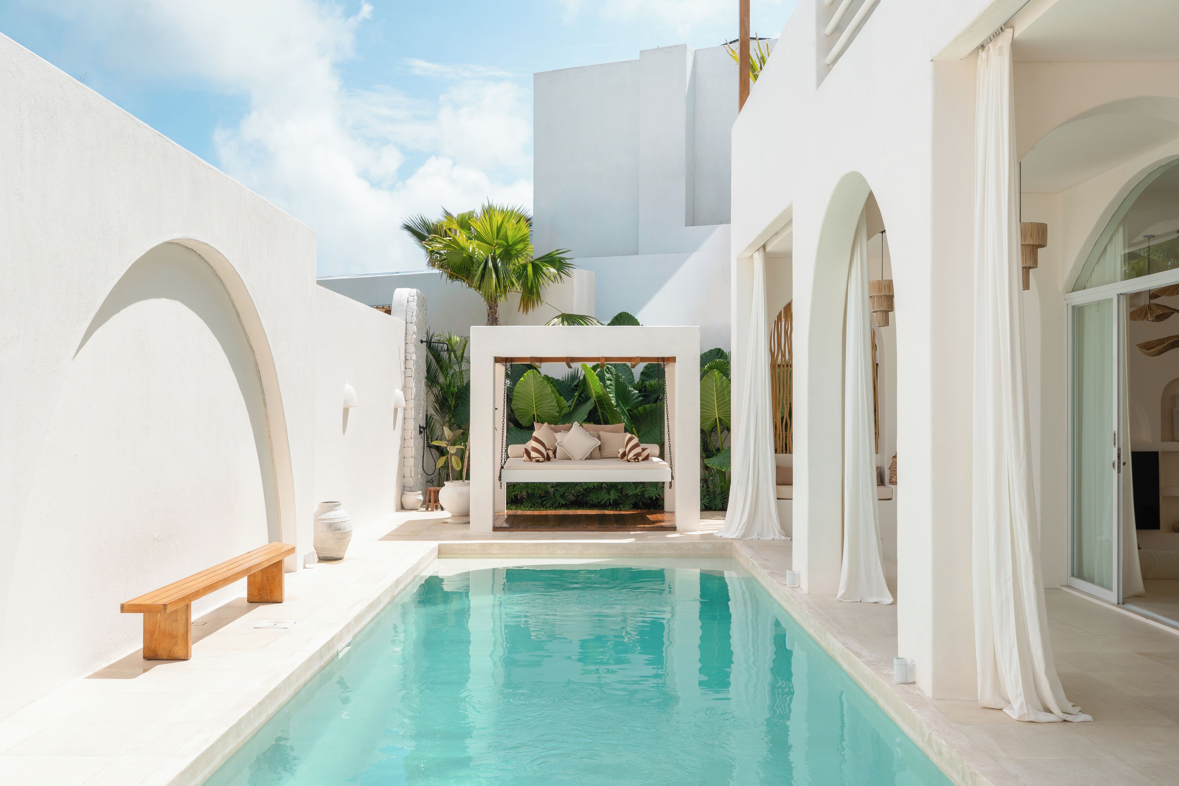 A modern pool area with a built-in seating area, surrounded by white walls and arches, and a clear blue pool.