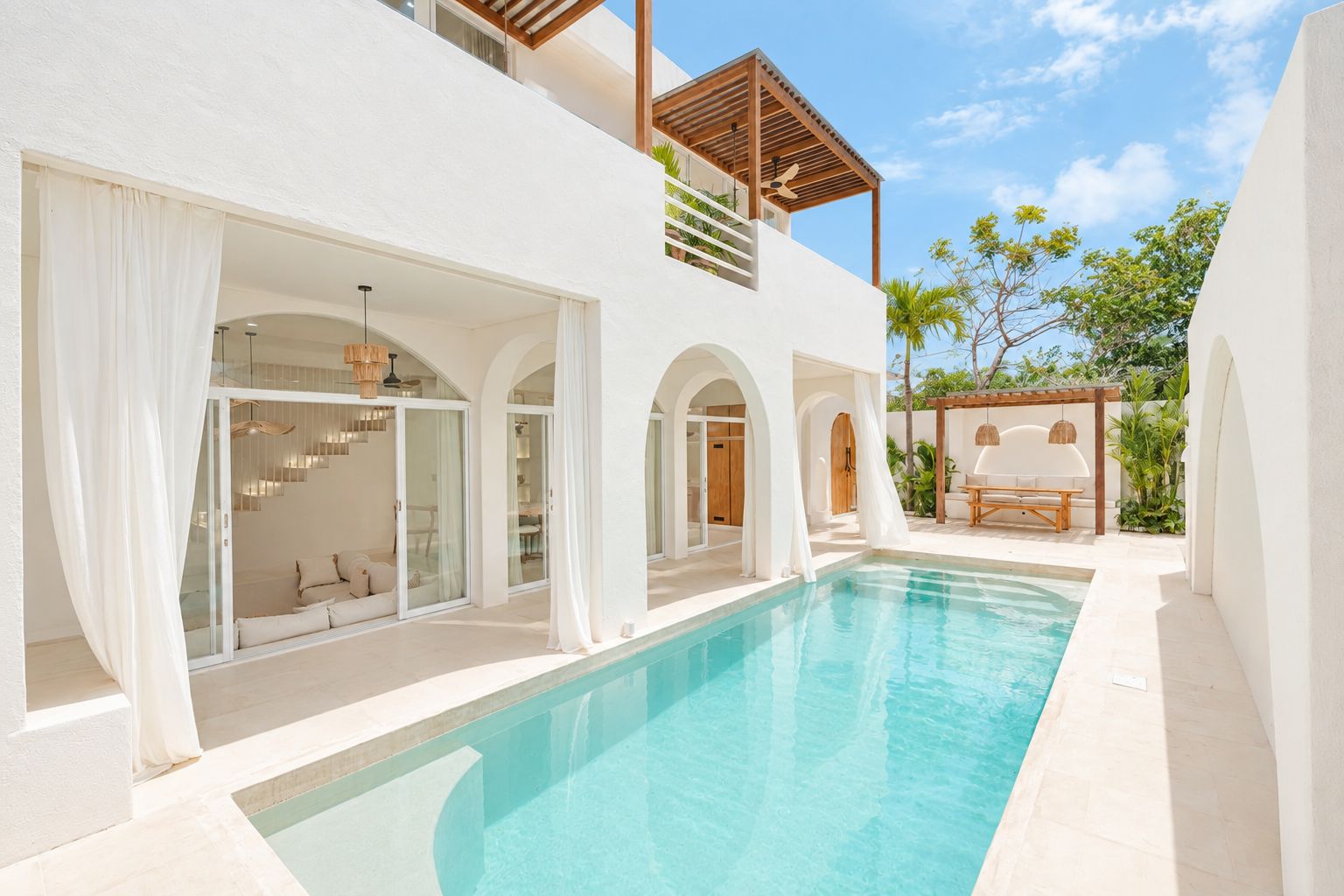 A modern poolside area with a clear pool, white walls, and a covered seating area.