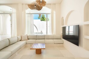 A modern living room with a large sectional sofa, a wooden coffee table, and a flat-screen TV mounted on the wall. - Villa Tomar El Sol by Alfred in Bali (Pecatu)