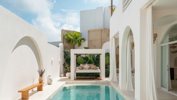Uma área de piscina com cadeira de balanço, banco e um pequeno jardim com plantas.
