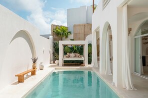 Uma área de piscina com cadeira de balanço, banco e um pequeno jardim com plantas.