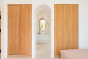 A hallway with wooden doors, a stone wall, and a bathroom with a sink and mirror.