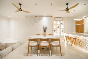 A modern dining area with a round table, wooden chairs, and ceiling fans.