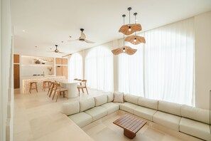 A modern living room with a sectional sofa, a dining area with wooden chairs, and a kitchen in the background.