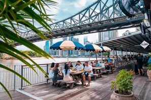 A rooftop bar with outdoor seating, overlooking a river and a bridge. - 2BR CBD Apartment with Rooftop Pool & Parking (Brisbane)