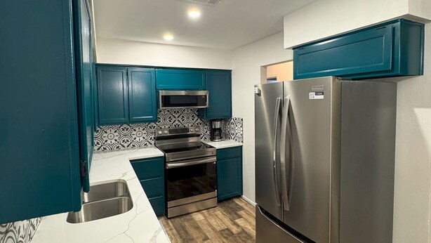 A modern kitchen with teal cabinets, a stainless steel refrigerator, a built-in oven, and a microwave.
