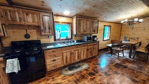 Cocina de cabaña de madera con estufa, pileta, alacenas y un comedor.