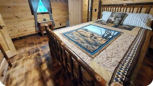 Un dormitorio de cabaña de madera con una cama, una mesita y una ventana con cortinas.