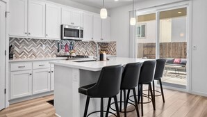 Une cuisine moderne avec des meubles blancs, un îlot central doté de tabourets, un four à micro-ondes et un dosseret orné d’un motif en chevrons.