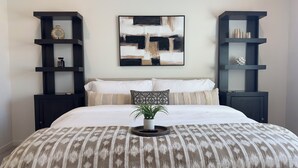 Une chambre à coucher avec un lit, un grand tableau abstrait et deux étagères noires ornées d’objets décoratifs.