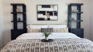 Una camera da letto con un letto, un quadro astratto di grandi dimensioni e due mensole nere con oggetti decorativi.