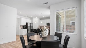 Une cuisine moderne avec des meubles blancs, un îlot central et un coin repas comprenant une table ronde et des chaises.