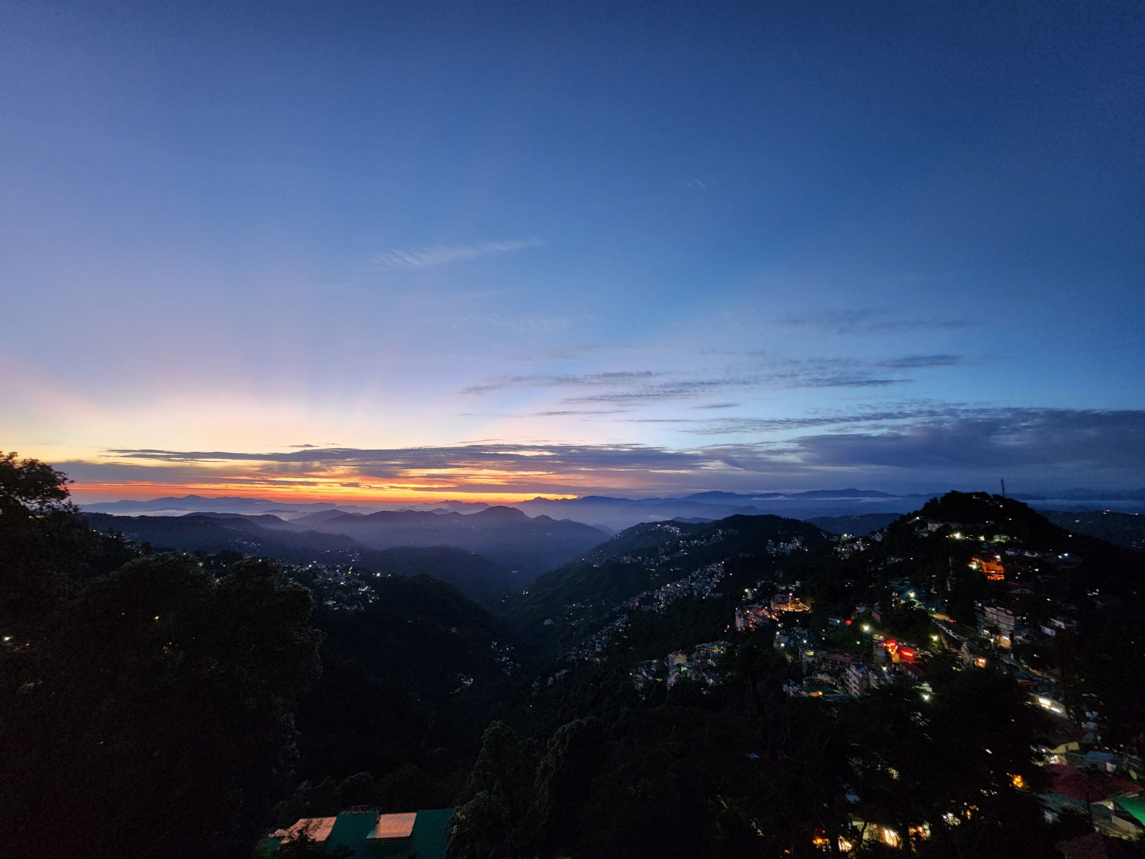 A mountainous landscape at dusk with distant city lights.