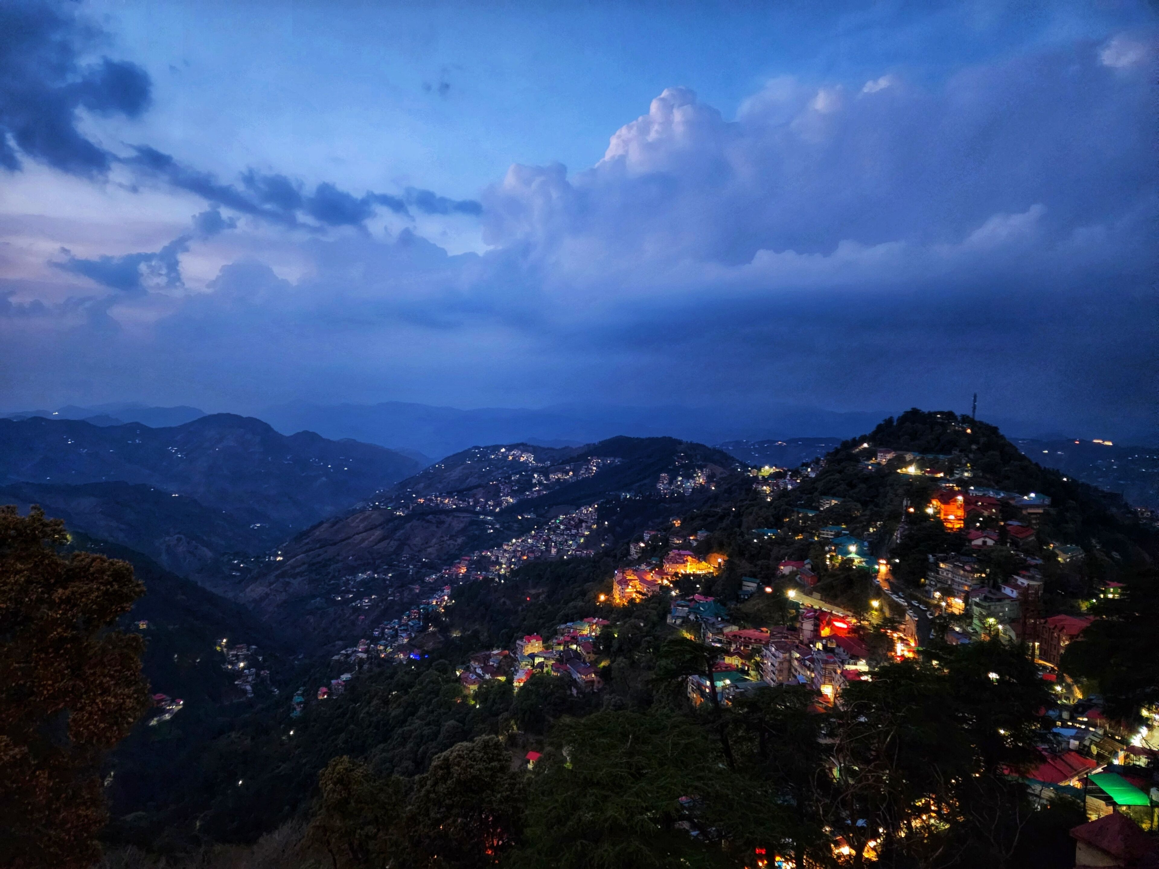 A mountainous landscape at dusk with a town illuminated by street lights.