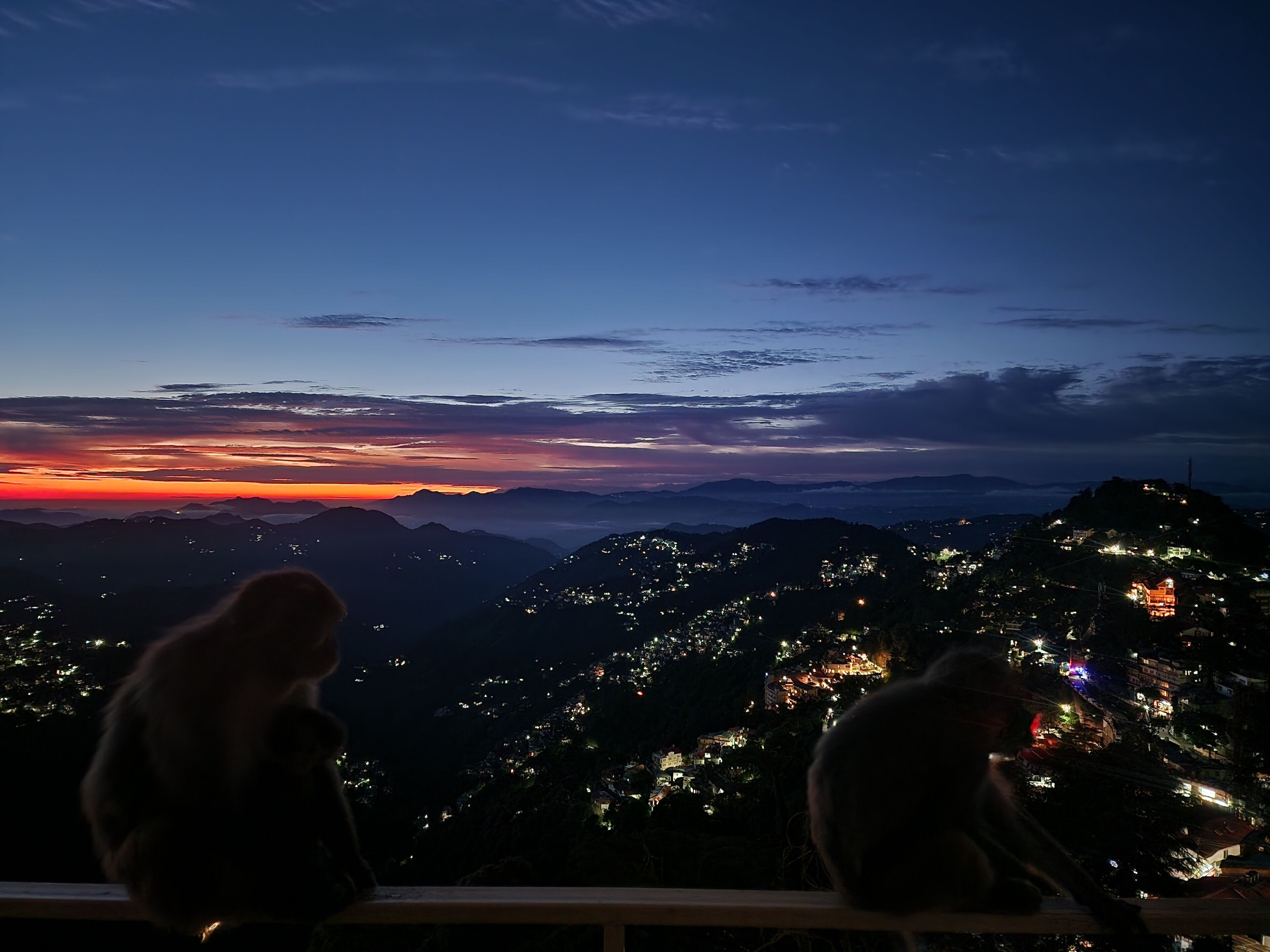 Une vue panoramique d’un paysage montagneux au crépuscule, avec les lumières de la ville qui scintillent au loin.