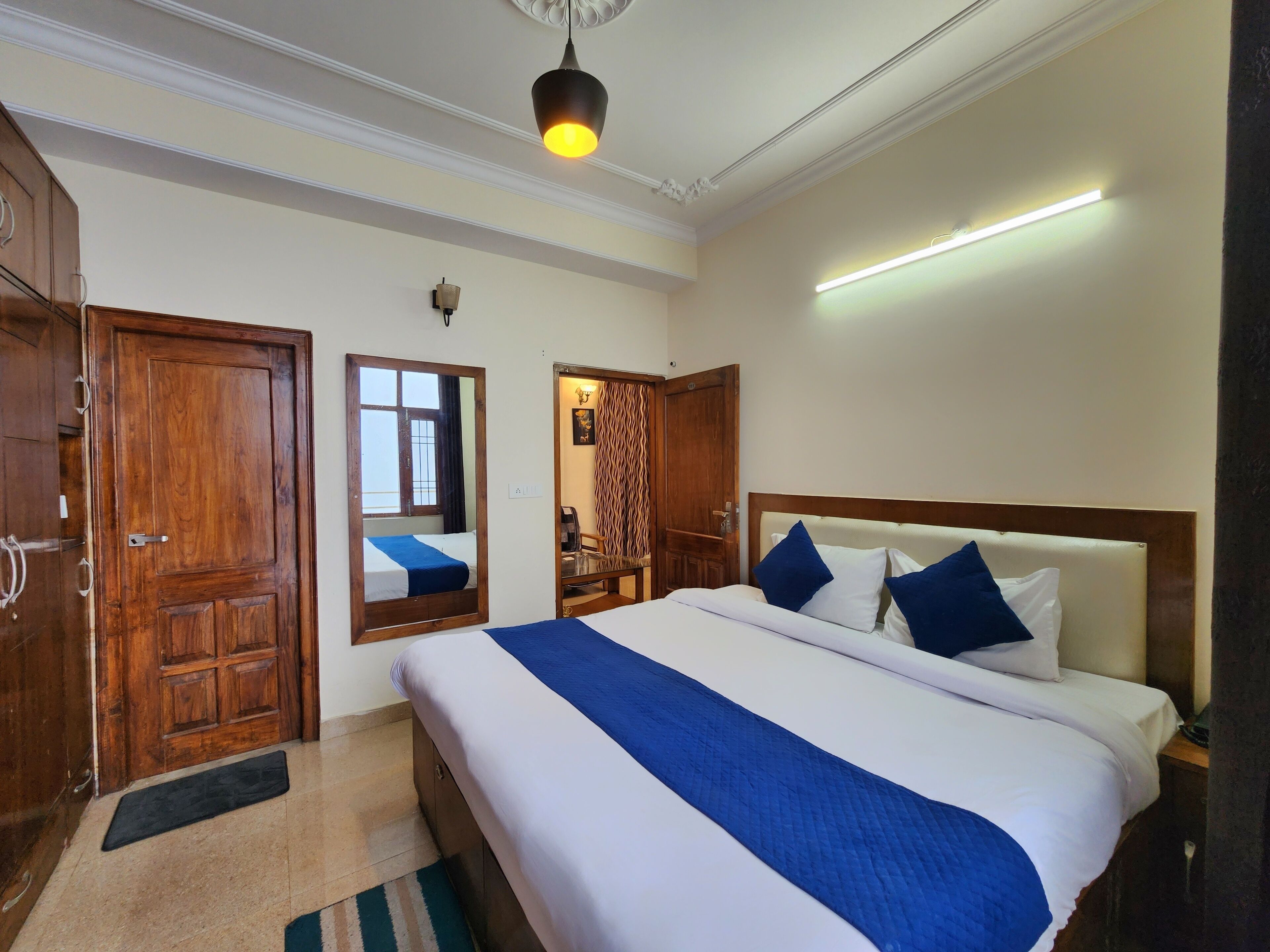 A hotel room with a large bed, wooden wardrobe, a mirror, and a modern light fixture.