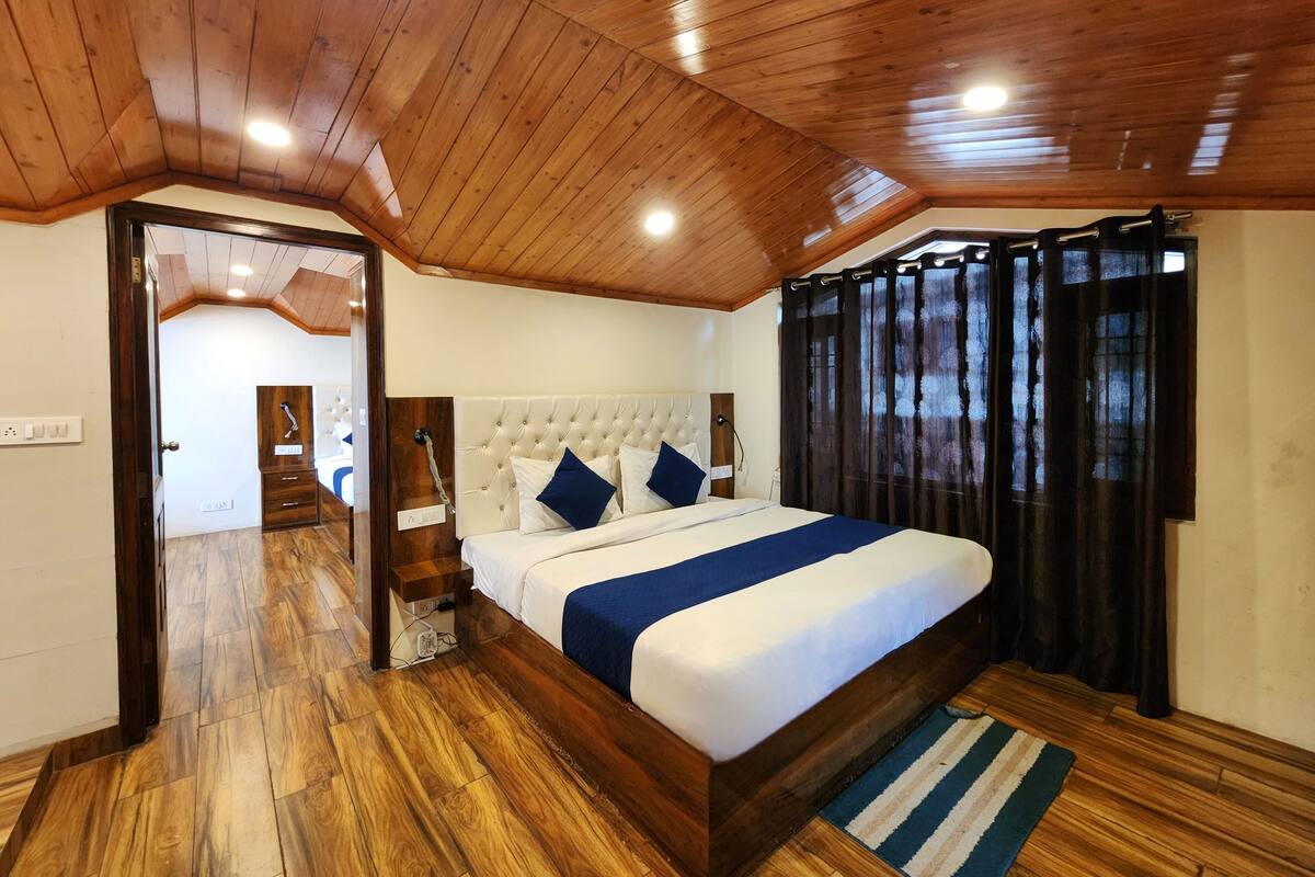 A bedroom with a wooden ceiling, a large bed with white bedding and blue accents, a wooden dresser, and a dark curtain.
