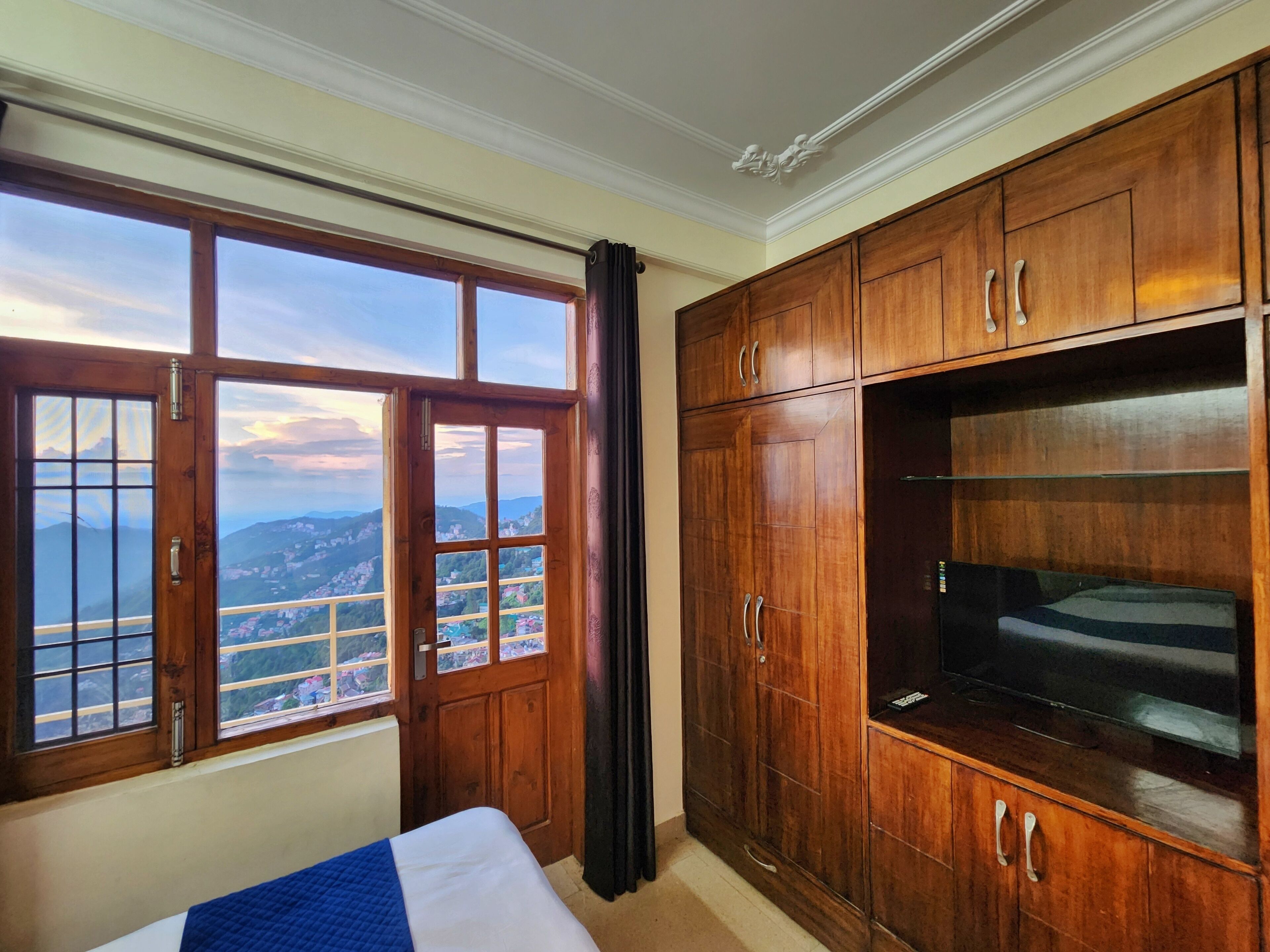 Ein Hotelzimmer mit großem Holzschrank, einem Bett mit blauer Decke und Blick auf eine Küstenlandschaft durch ein großes Fenster.