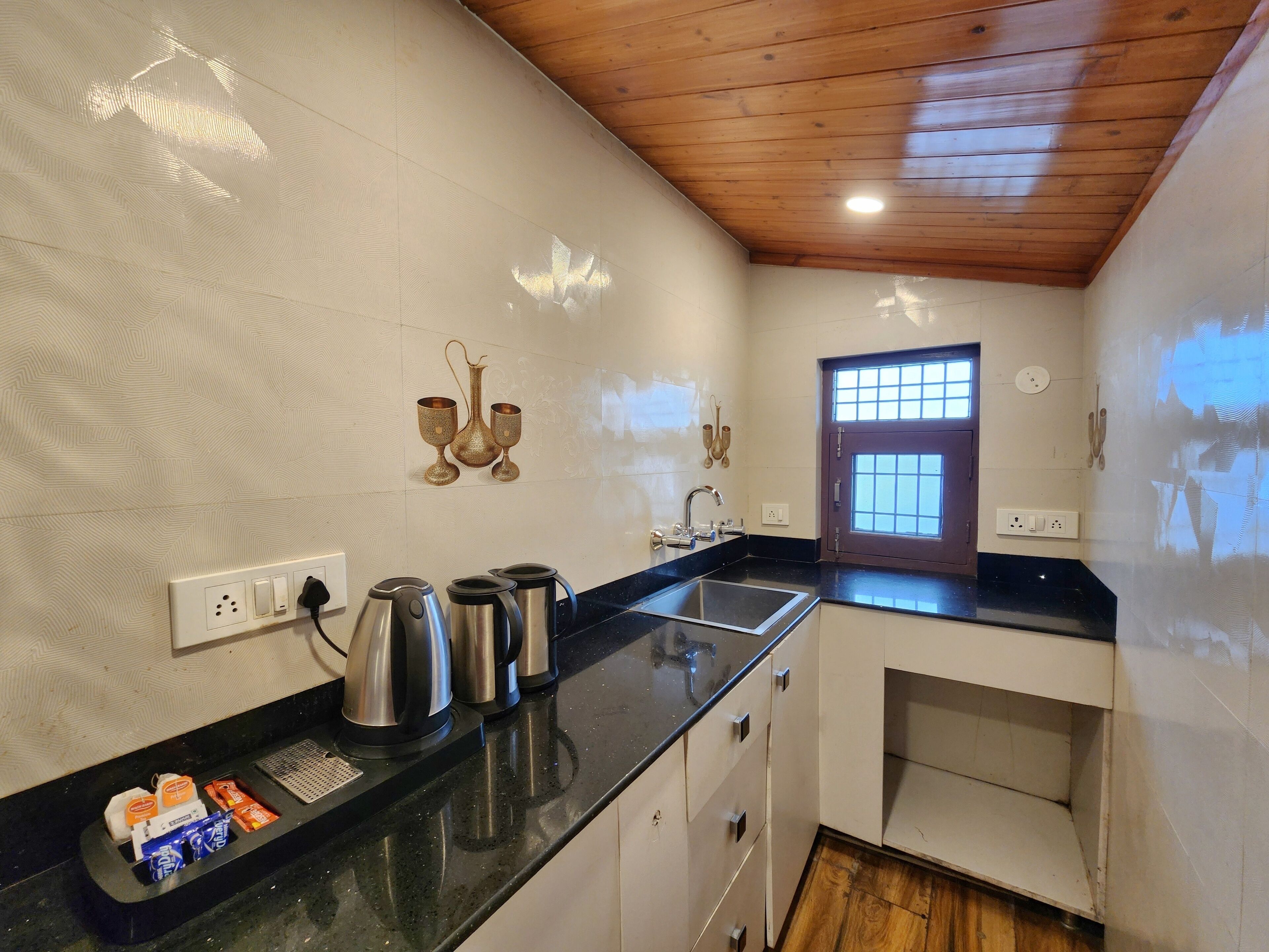 Una cocina con cubierta negra, electrodomésticos de acero inoxidable, una ventana con diseño de cuadrícula y techo de madera.