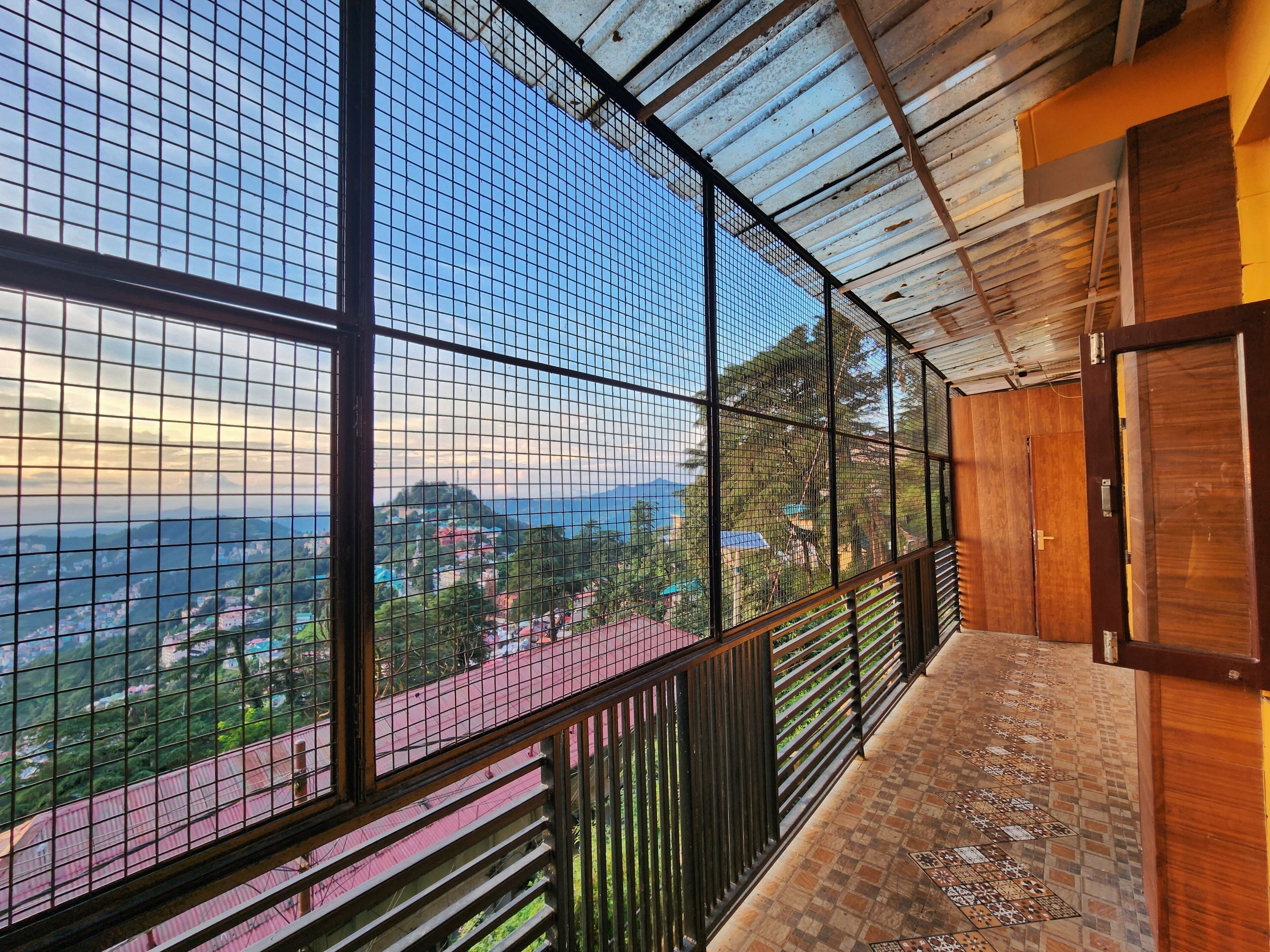 A balcony with a metal grid railing, a tiled floor, and a view of a mountainous landscape.