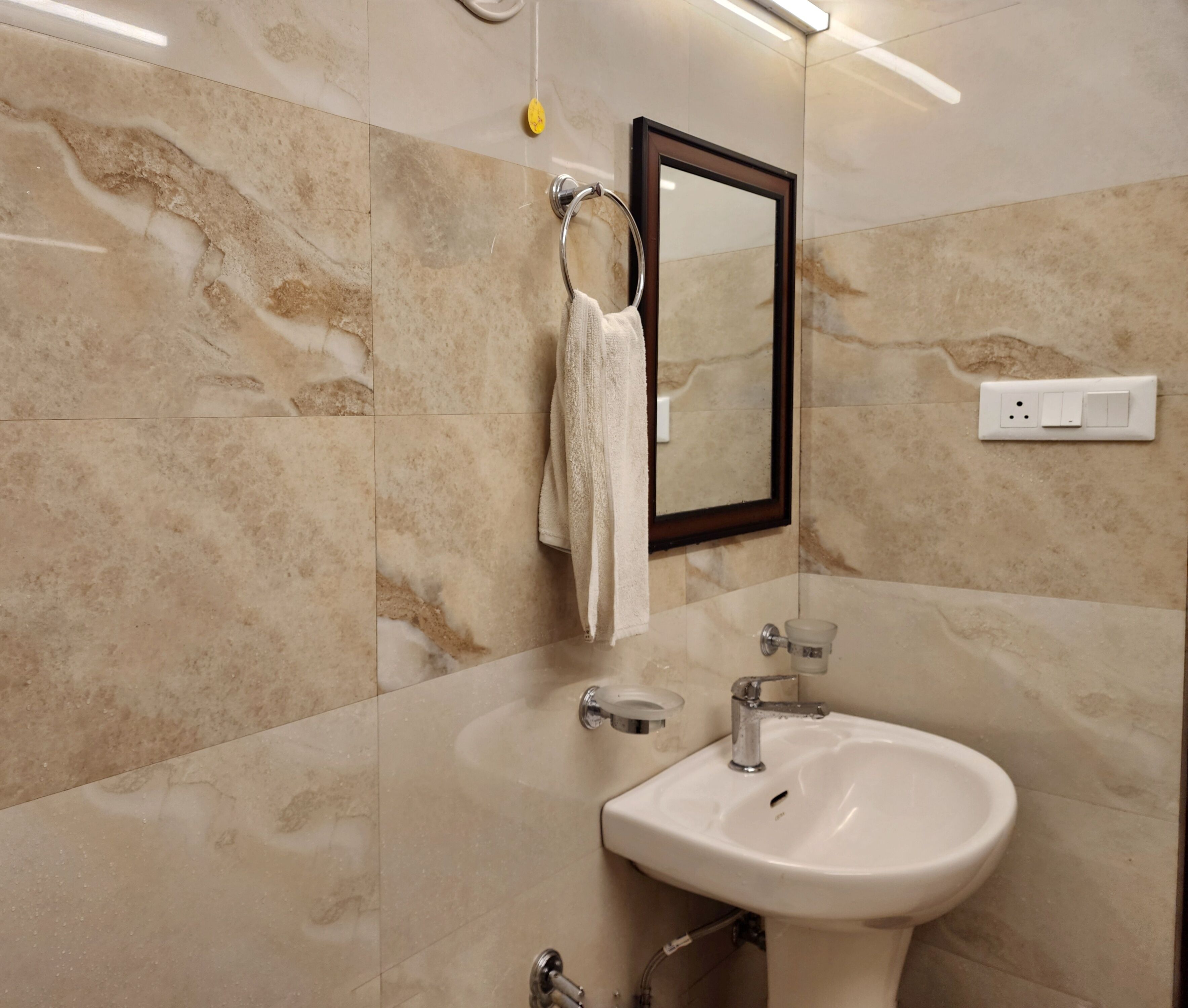 Une salle de bain avec un lavabo blanc, un porte-serviettes, un miroir et un interrupteur sur le mur.
