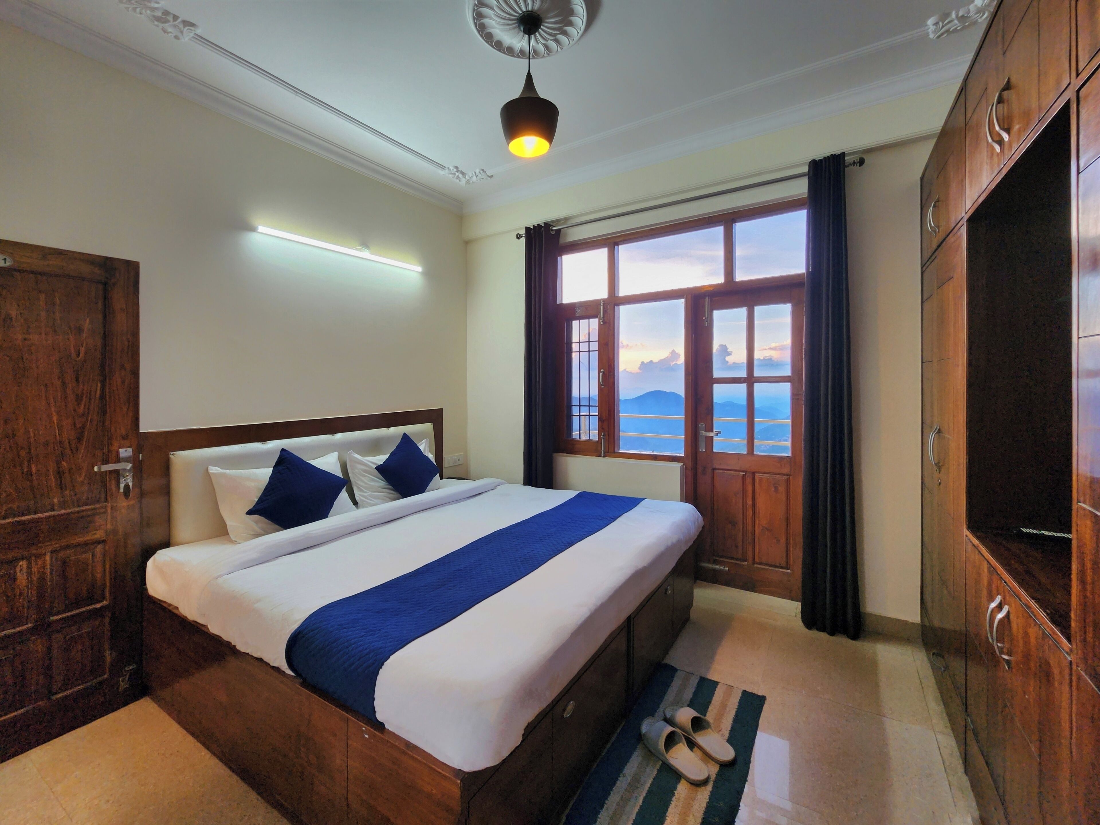Une chambre d’hôtel avec un grand lit, une armoire en bois et une vue sur les montagnes par la fenêtre.