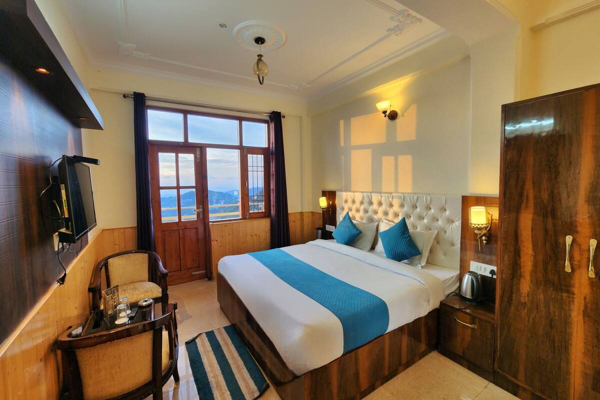 A hotel room with a large bed, wooden furniture, a TV, and a view of the mountains.